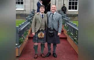 Two men in kilts standing together, looking at the camera and smiling