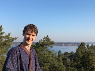 A man in a kimono smiling for the camera, with a backdrop of rural Japan