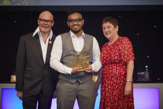 A man posing with an award beside two other people