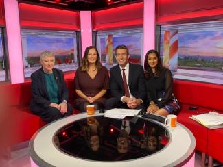 Four people sitting on a sofa in a TV studio, smiling for the camera