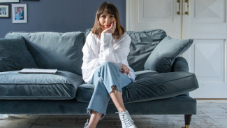 A woman sitting on a sofa with her legs crossed and her head in her hand, looking at the camera