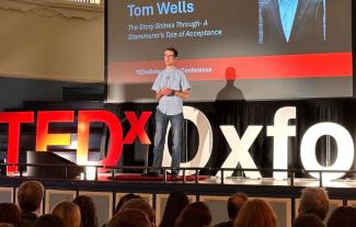 A young man on a stage speaking publicly to an audience