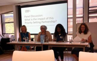 Four women sitting at a desk in front of a powerpoint presentation slide