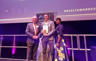 A man on a stage holding an award, with a man and a woman either side of him