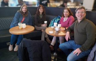 Four people sitting in a coffee shop, smiling