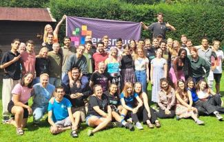 A big group of people, huddled together and smiling, some standing, some sitting and crouching