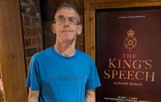 A man smiling in front of a poster with the words 'The King's Speech'