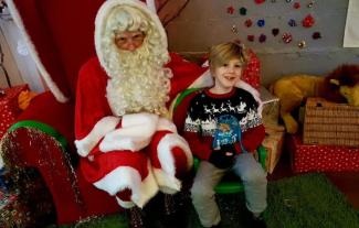 A young boy sitting next to Father Christmas