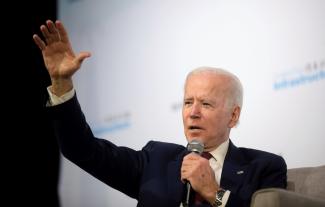 President Joe Biden speaking into a microphone and waving