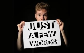 A man holding a sign up to cover his mouth. The sign reads 'Just a few words'