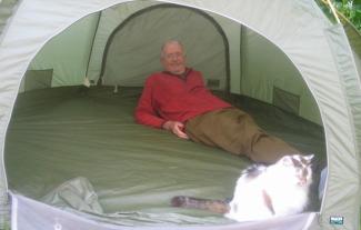 A man lying inside a tent, with a cat in front of him