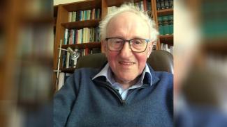 An elderly man in front of a bookcase smiling