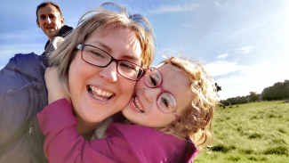 A young girl embracing her mother as they both smile for the camera, in a park