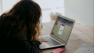 A girl using a laptop computer. Her face is obscured.