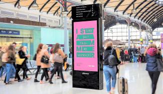 People on a railway station platform walking around an advertisement display