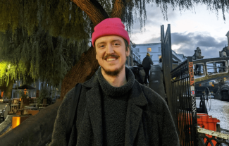 A man in a woolly hat smiling, next to a canal