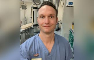 A man in a hospital uniform and setting, smiling