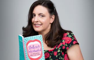 A woman holding a book and looking at the camera, smiling