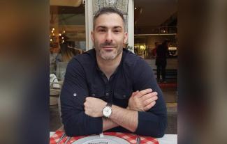 A man at a restaurant table, looking at the camera with his arms crossed