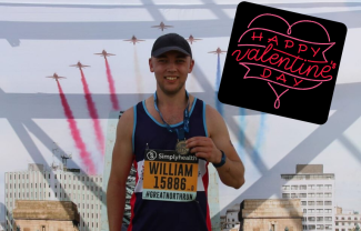 A  man in running gear showing a medal to the camera and smiling. Behind him are Red Arrow aeroplanes leaving trails in the sky.