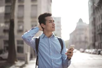 A man in a street, holding a phone, with his other hand on the back of his head