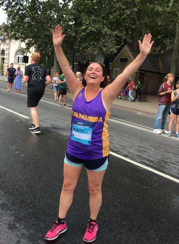 A woman in running gear standing with her hands aloft, smiling