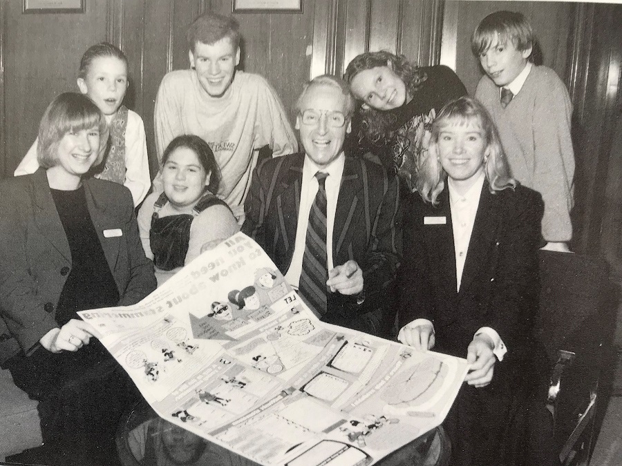 A man holding a poster, next to a woman and a group of children, all looking at the camera and smiling.