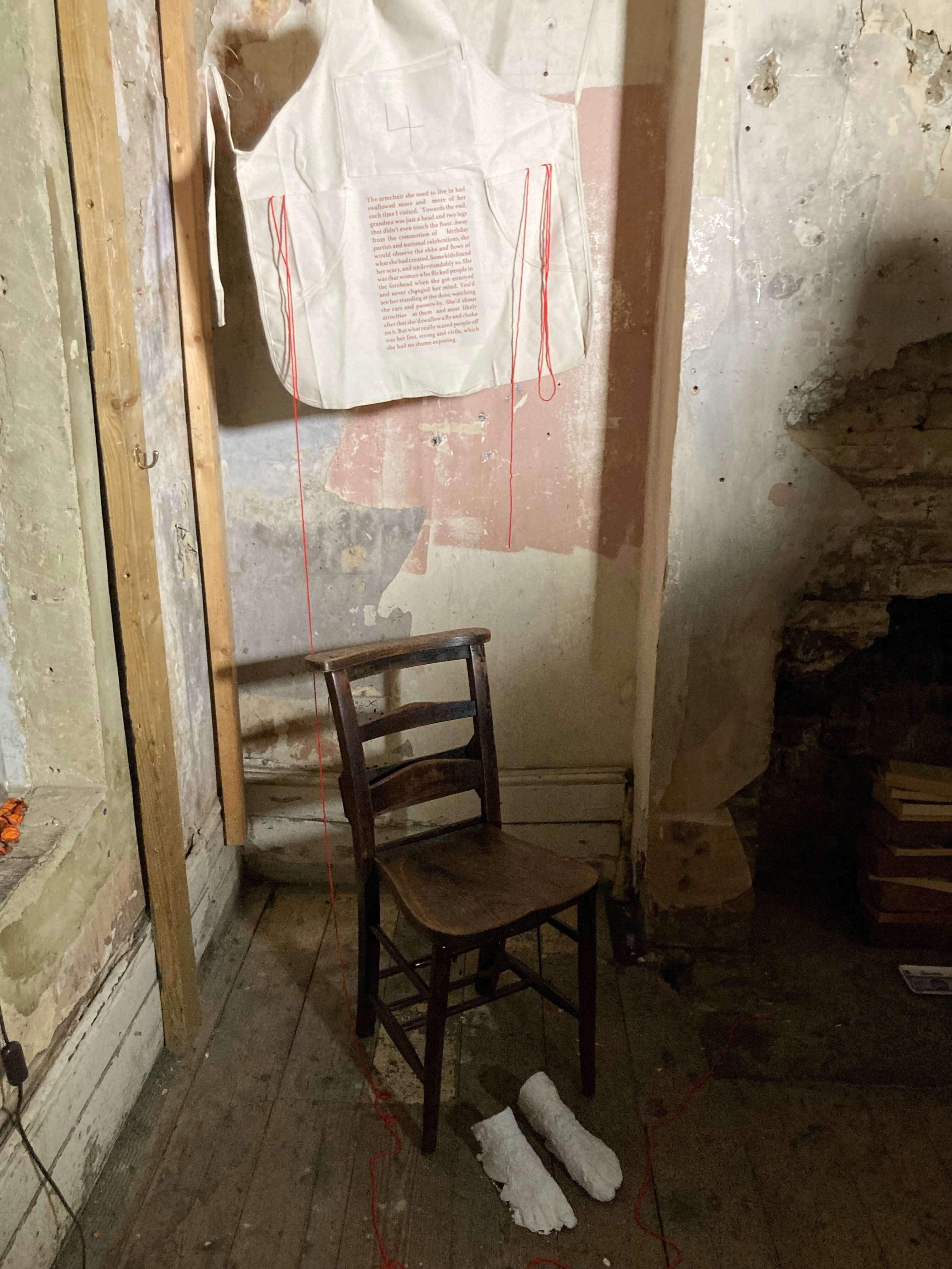 An art exhibit showing a chair next to a wall that has a sheet of paper with writing on it.