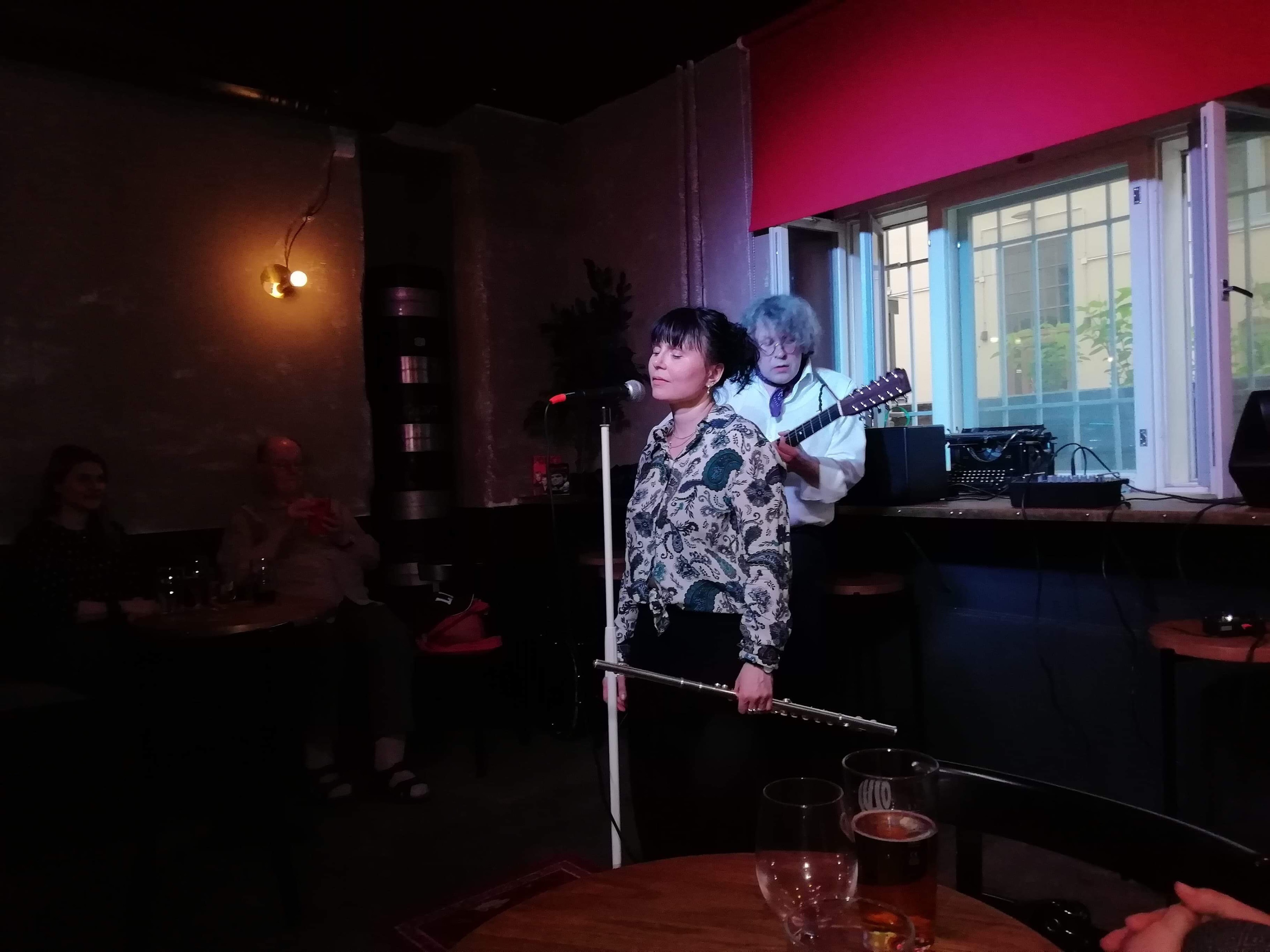 A woman singing into a microphone with a man playing the guitar behind her