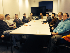 A group of people sat round a table, all looking at the camera